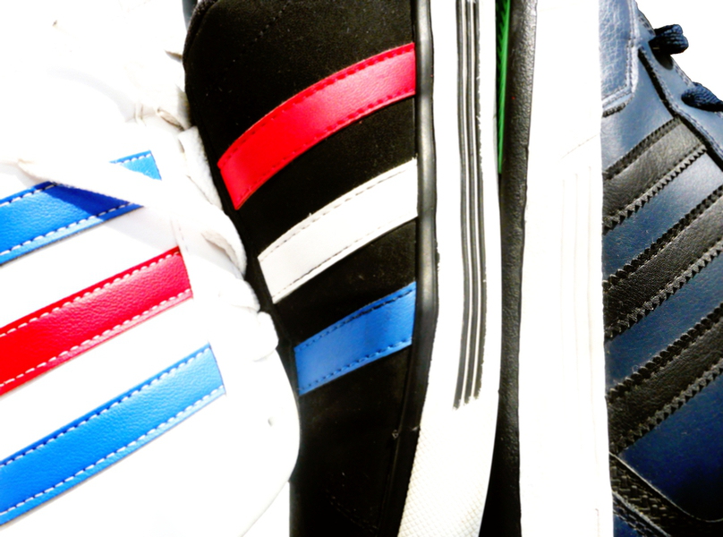 Bildausschnitt dreier verschiedenfärbiger Adidas-Schuhe mit den drei seitlichen Streifen in unterschiedlicher Farbe